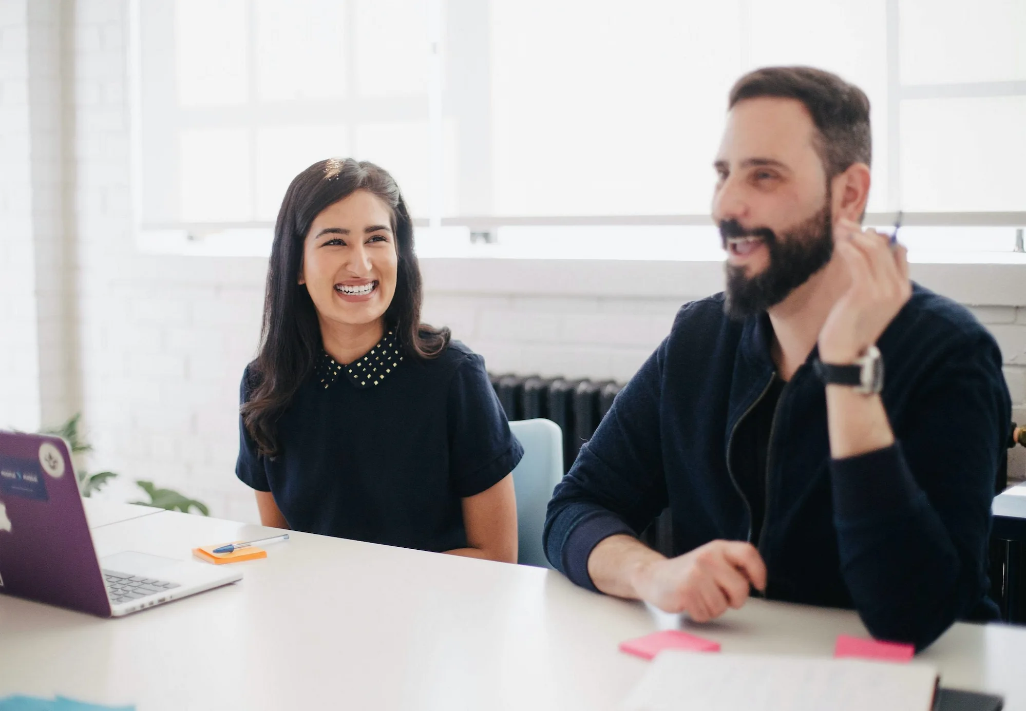  A man and woman working together at a table with a laptop in an office setting.
