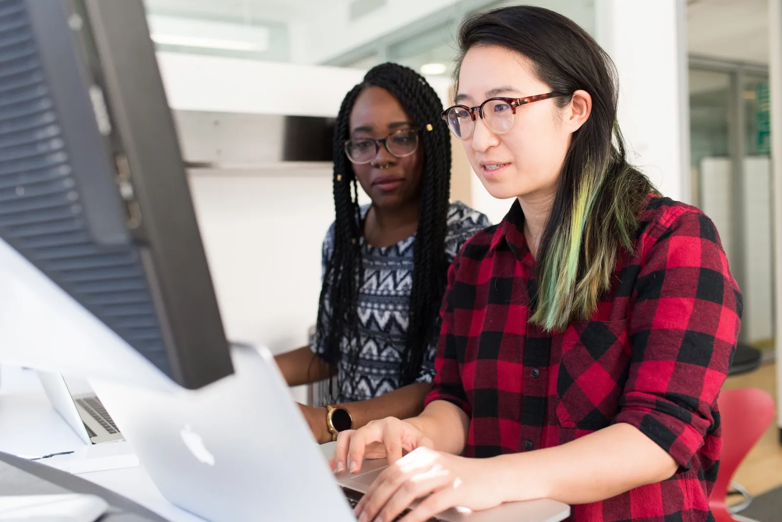 Two women wearing glasses collaborate on a computer, focused on tasks related to payroll and human resources management.