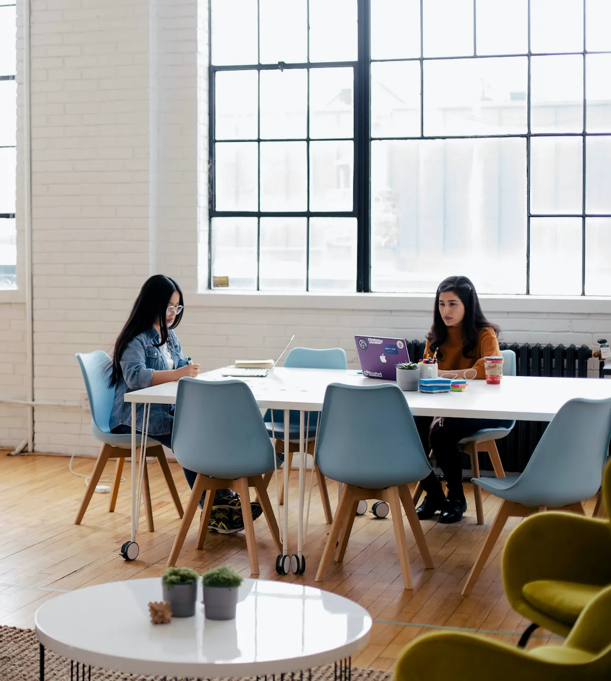 Two women collaborate at a table in an office setting, focused on their work.