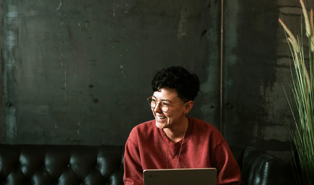 A woman sitting on a couch in an office workspace, using a laptop for work or personal tasks.
