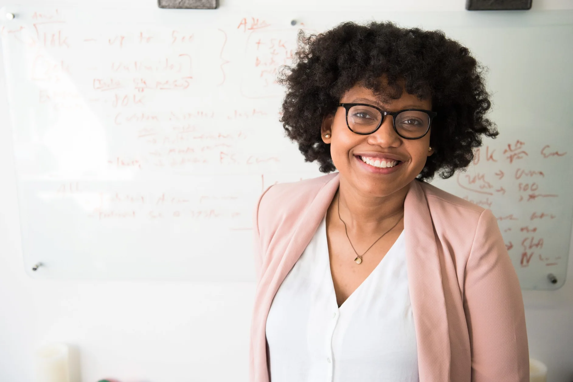 A woman in glasses and a pink jacket stands by a whiteboard, discussing independent contractor compliance services.