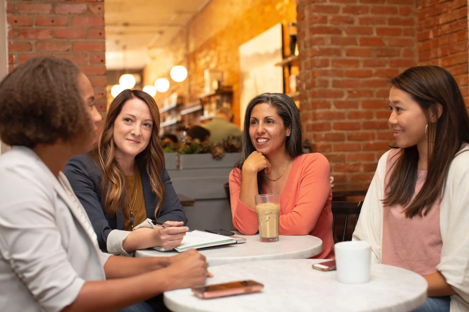 Four women seated at a cafe table, discussing staffing and recruiting topics in a cozy setting.